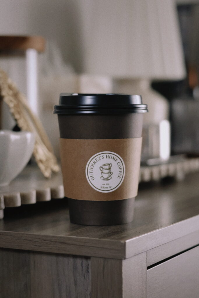 brown to go cup with black top and a cardboard color sleeve with a custom home cafe sticker